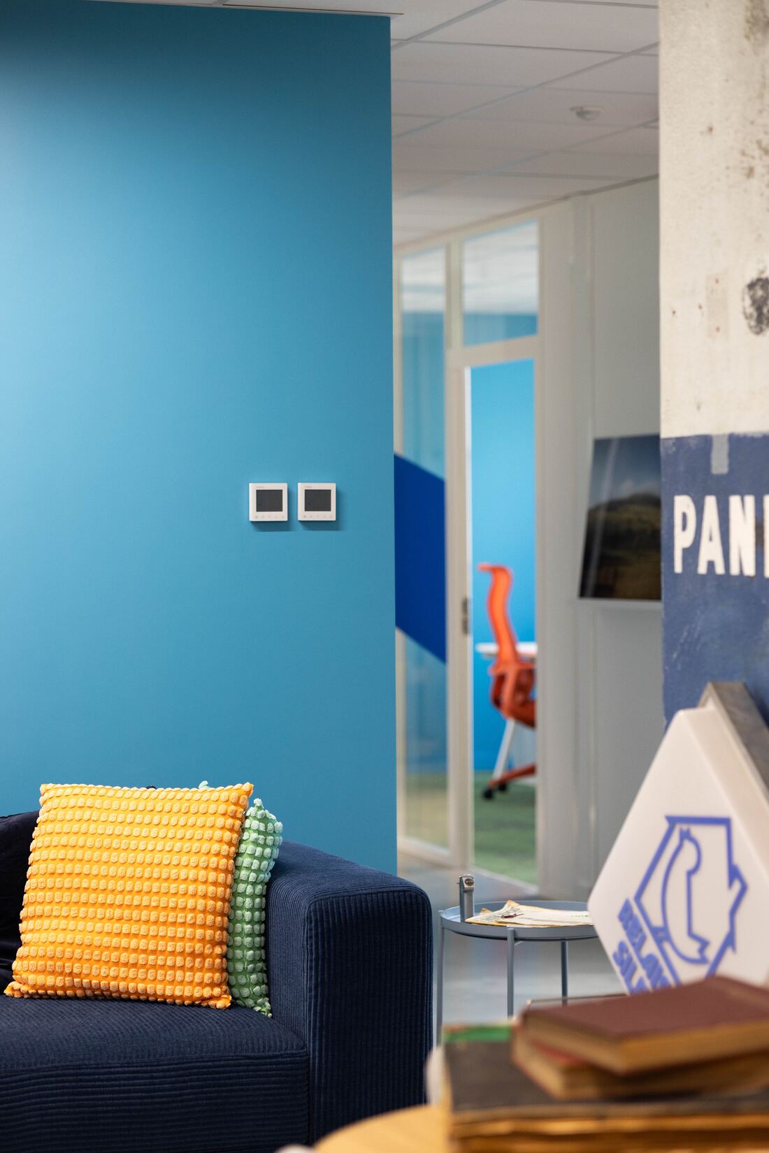 Espace de travail aux murs bleus, avec un canapé bleu marine et un coussin orange