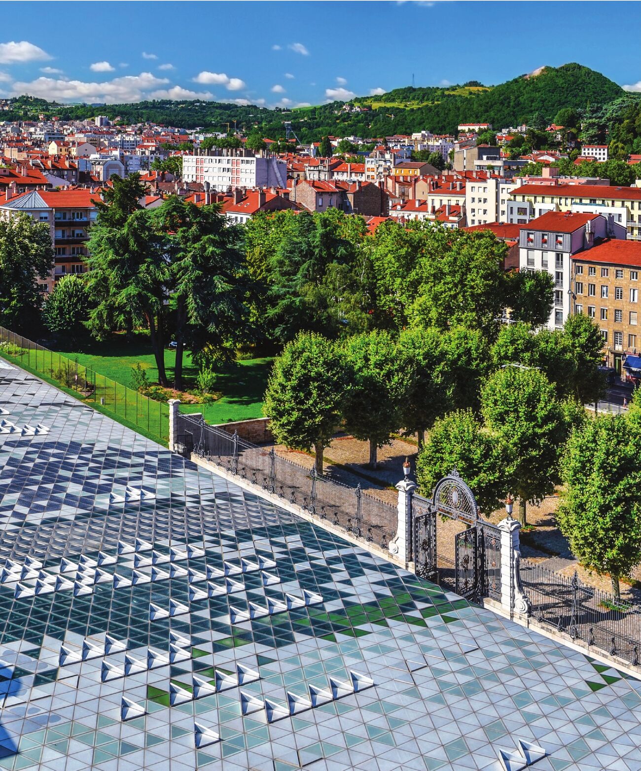 Toits de Saint-Étienne et parc arboré, vus d'en haut, avec une grande toiture vitrée à motifs triangulaires