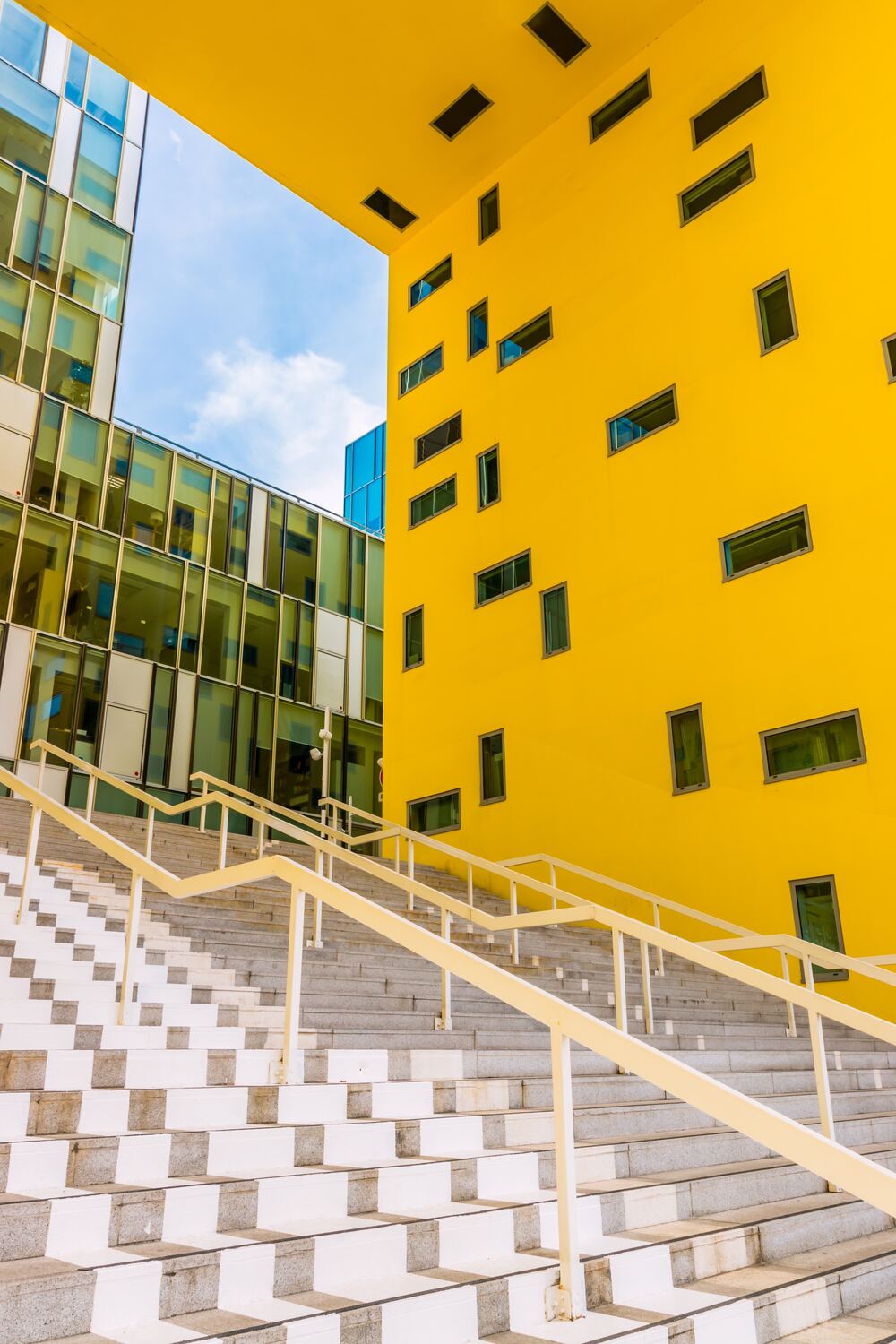 Immeuble de bureaux jaune et vitré, avec un grand escalier extérieur sous un ciel bleu