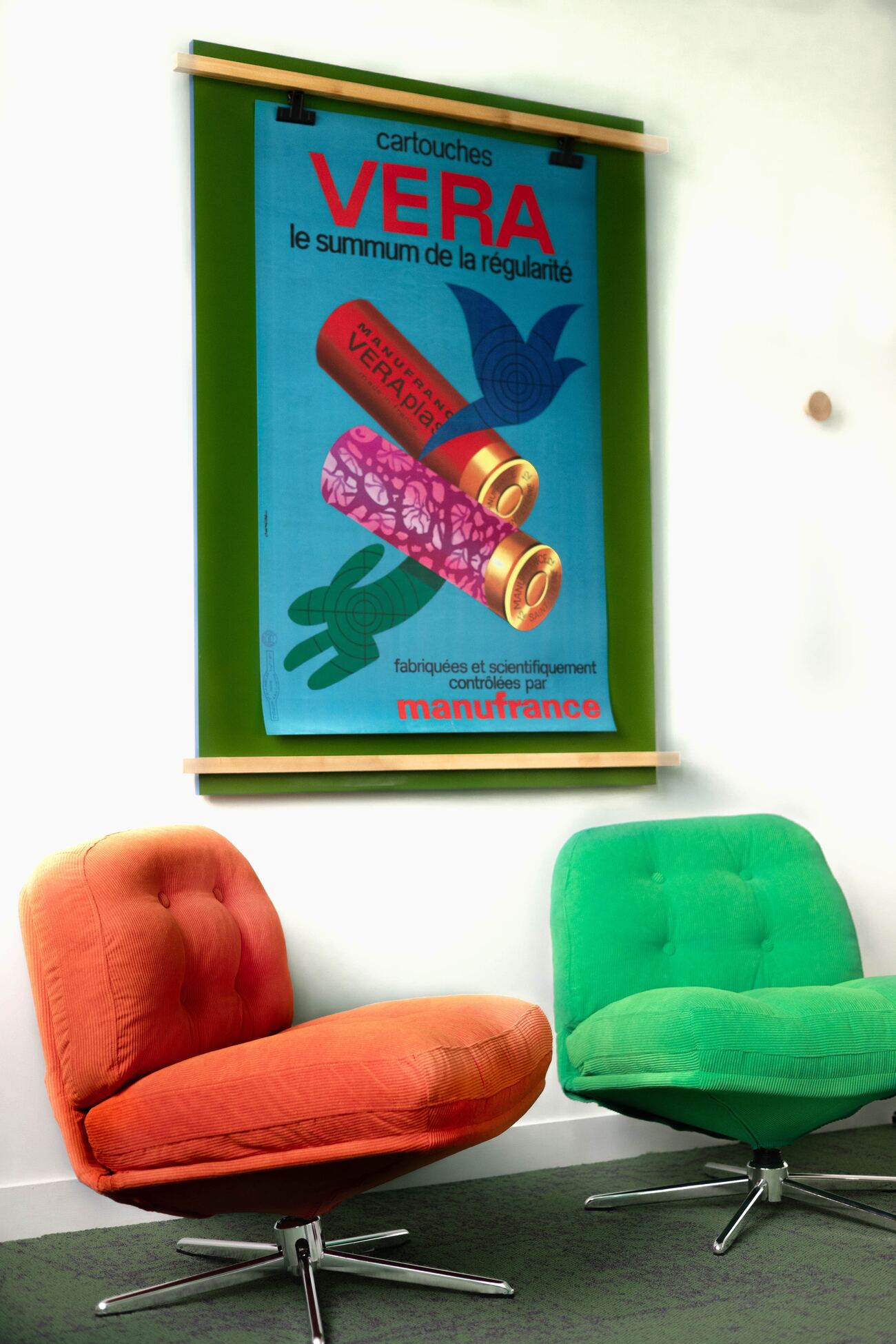Deux fauteuils vintage, orange et vert, sous une affiche Manufrance
