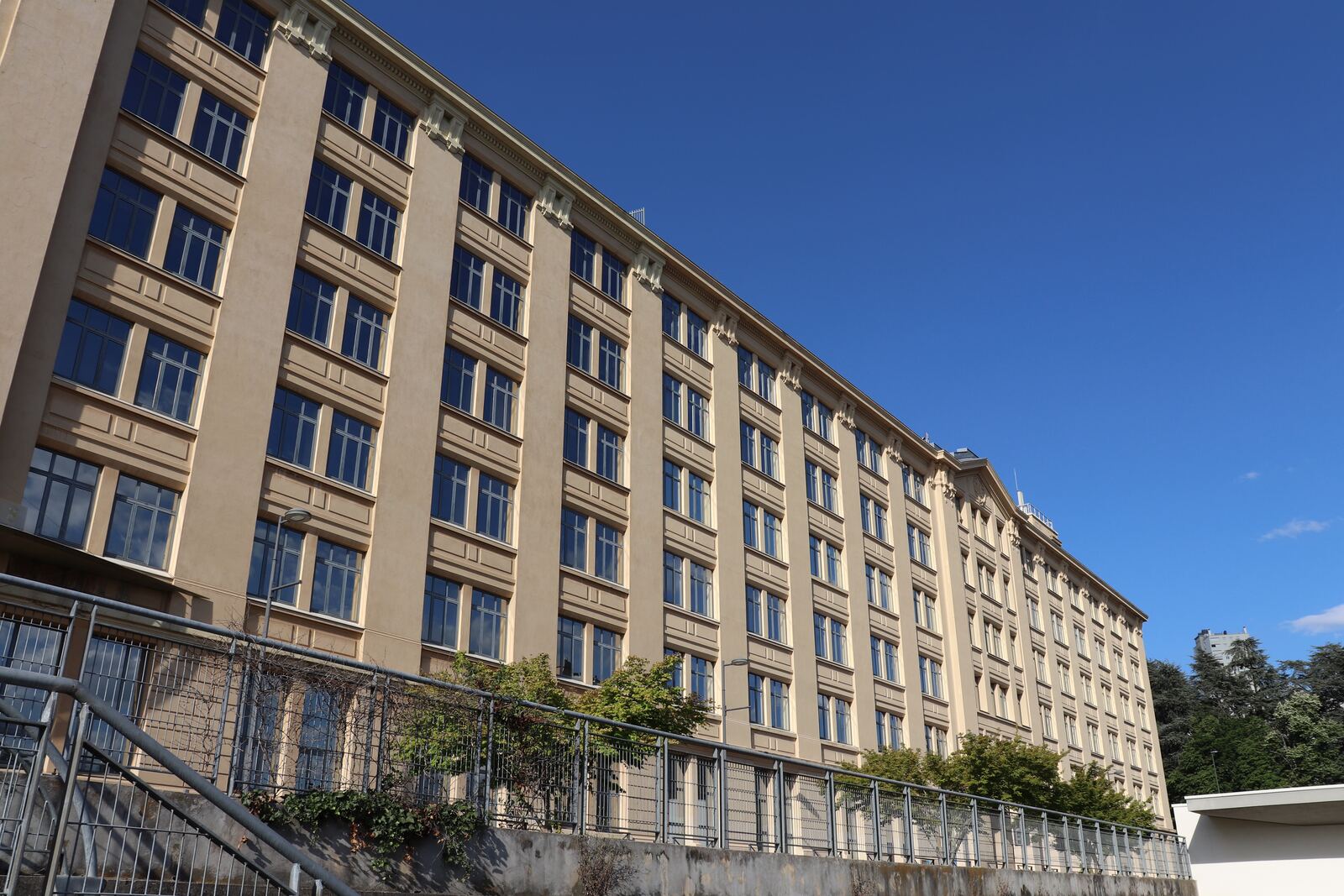 Façade claire d'un long immeuble de bureaux sous un ciel bleu, vue en perspective
