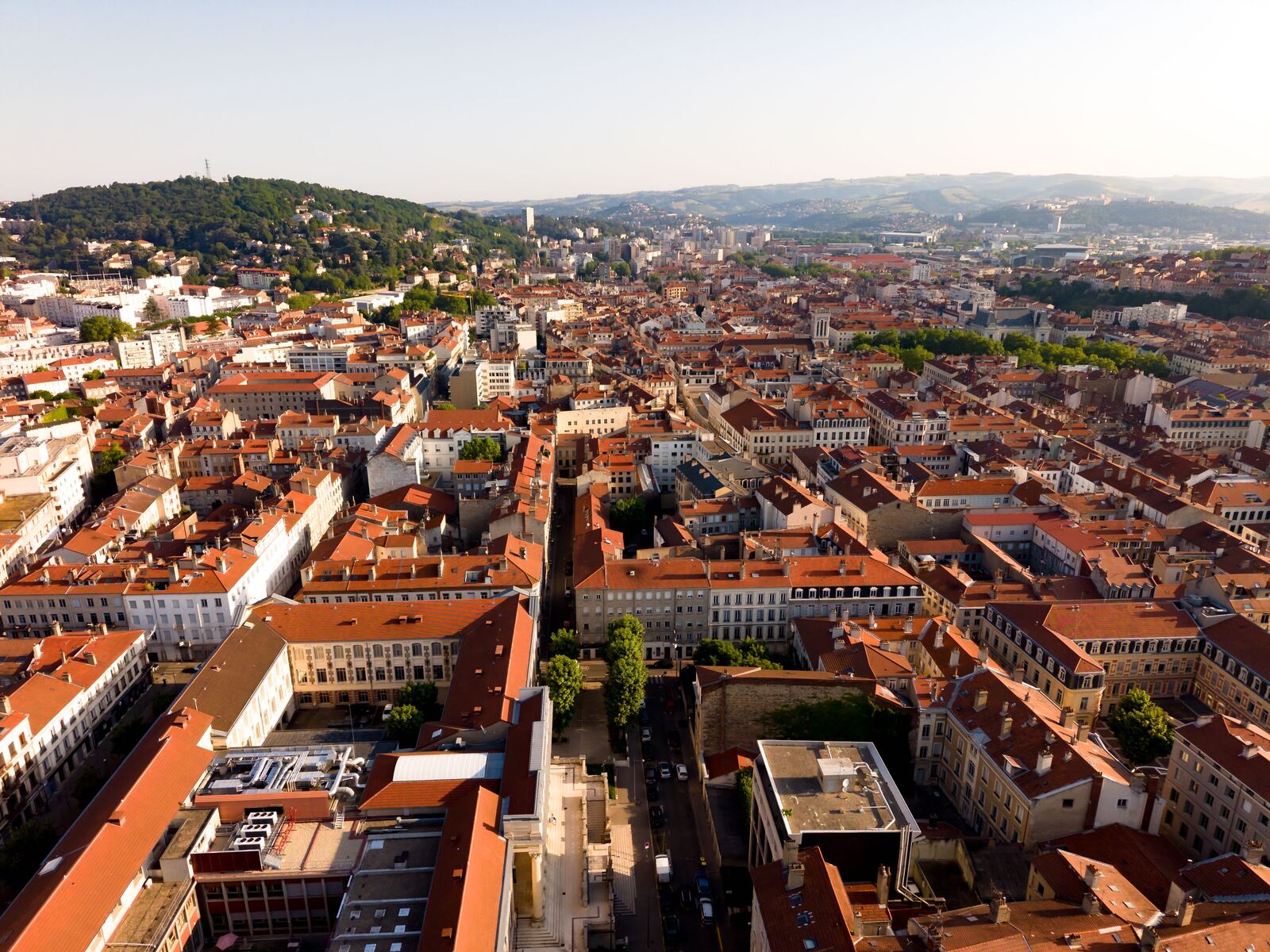 Vue aérienne du centre de Saint-Étienne : toits rouges et façades claires, avec la colline au fond