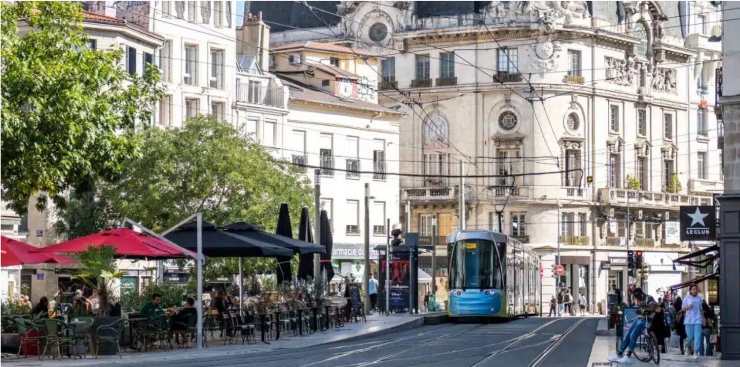 Une rue du centre de Saint-Étienne avec terrasses de café et tramway bleu devant des immeubles anciens