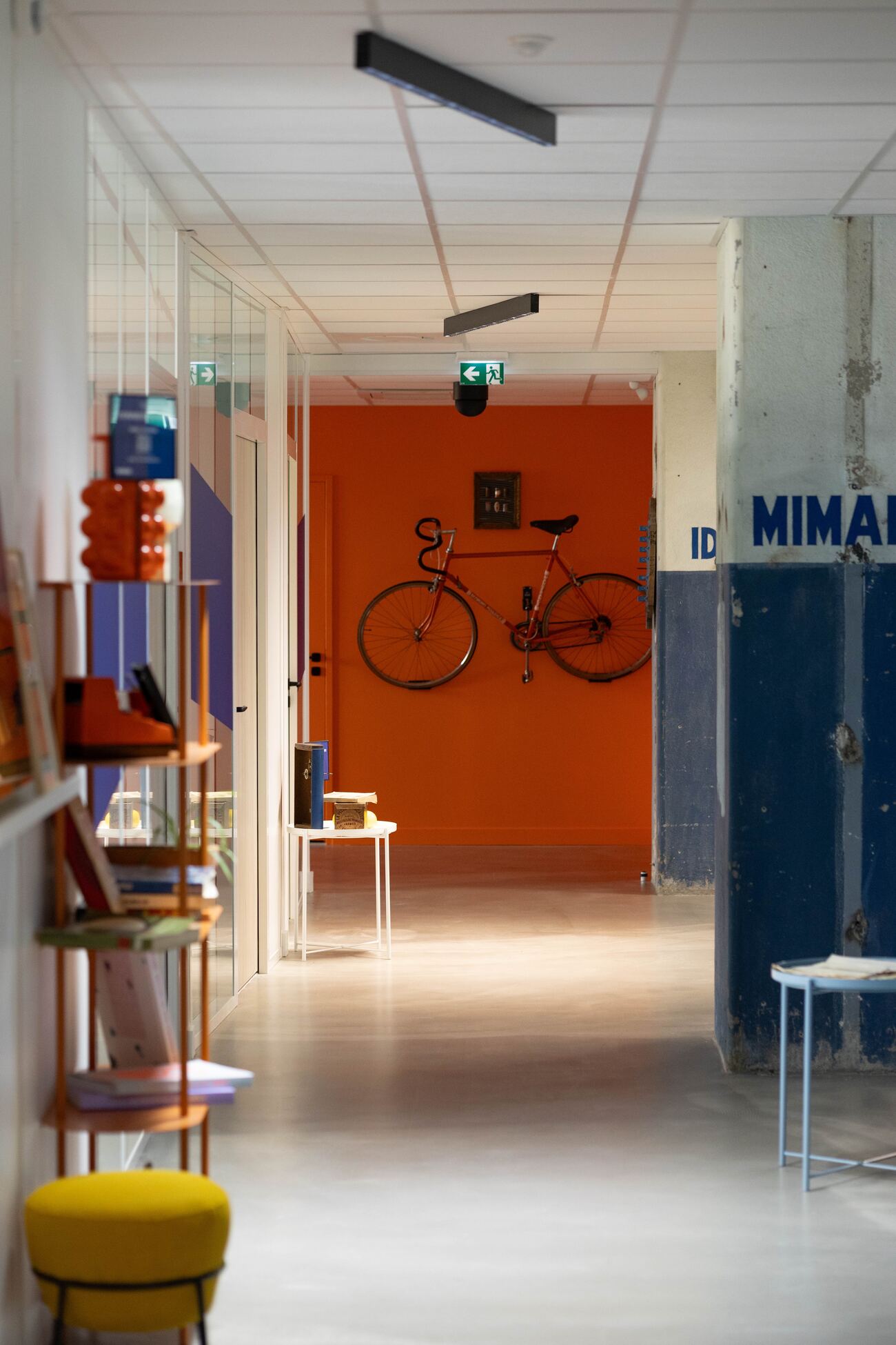 Couloir d'un bureau aux murs orange, avec un vélo accroché au mur et une étagère de livres