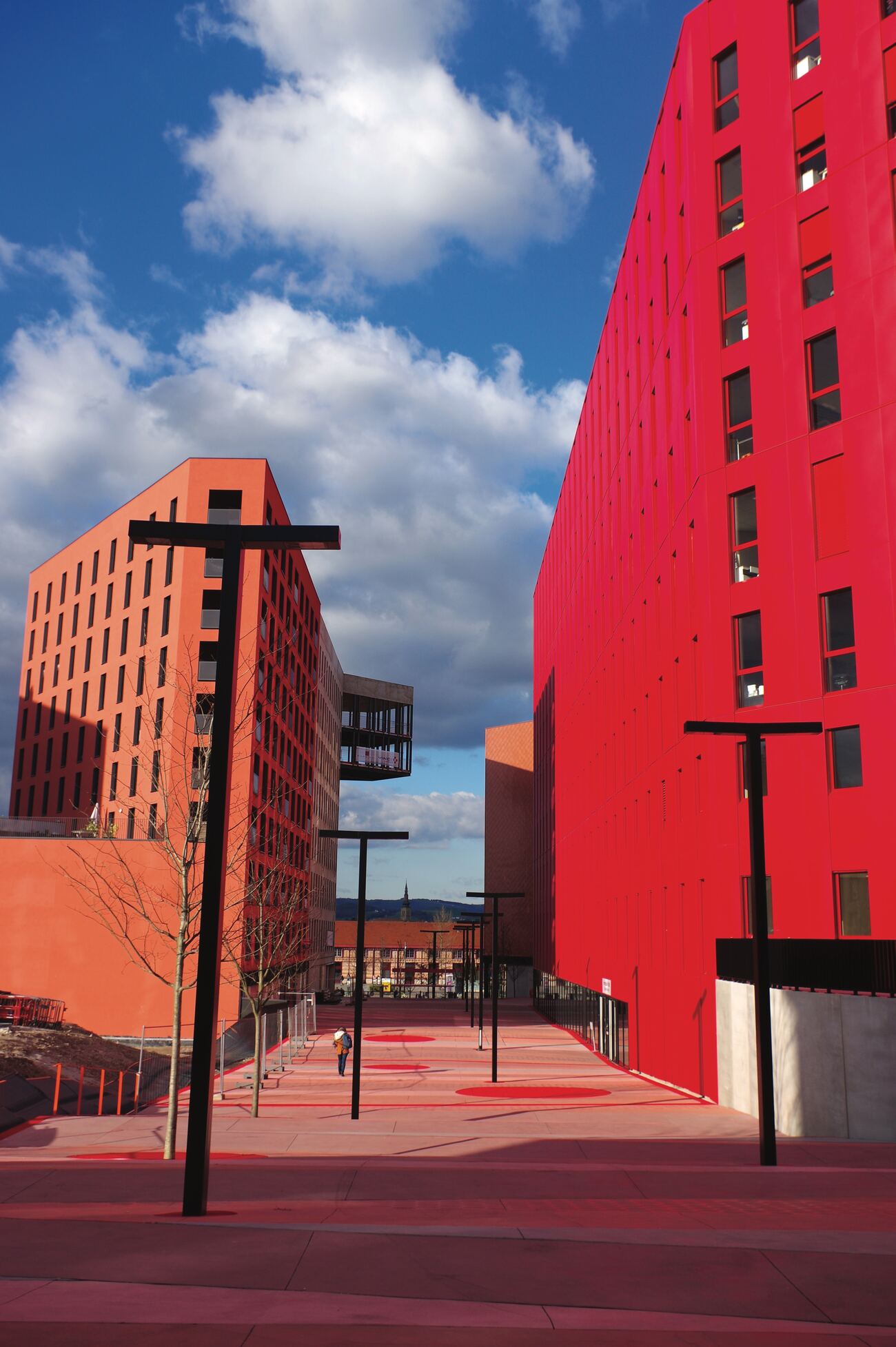 Deux immeubles rouges et orange séparés par une allée piétonne, sous un ciel nuageux