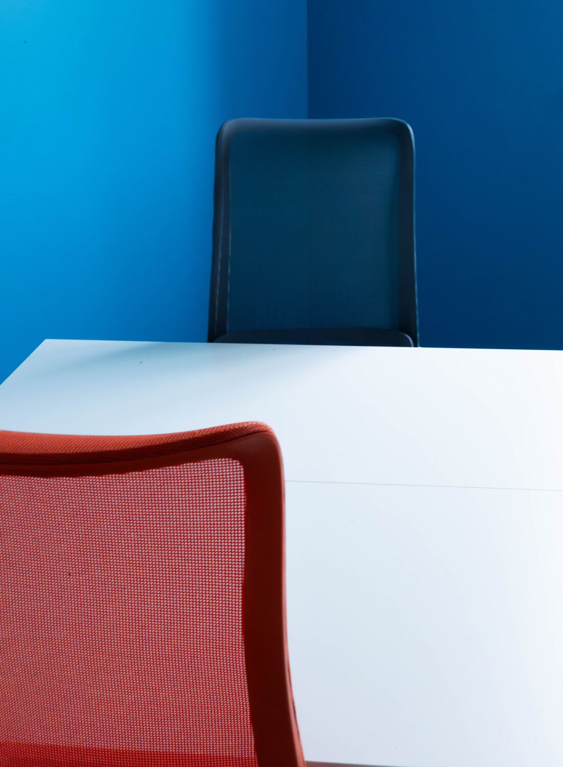 Gros plan sur un fauteuil bleu et un fauteuil rouge devant une table blanche, sur un mur bleu