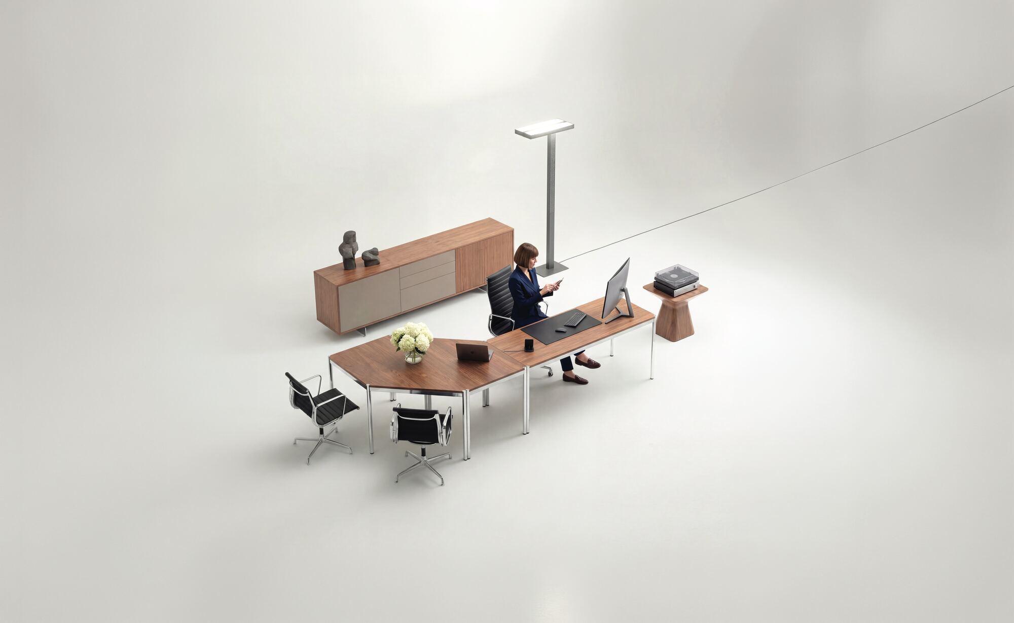 Vue en plongée d'un bureau en bois, d'un buffet et de deux fauteuils, dans une pièce blanche