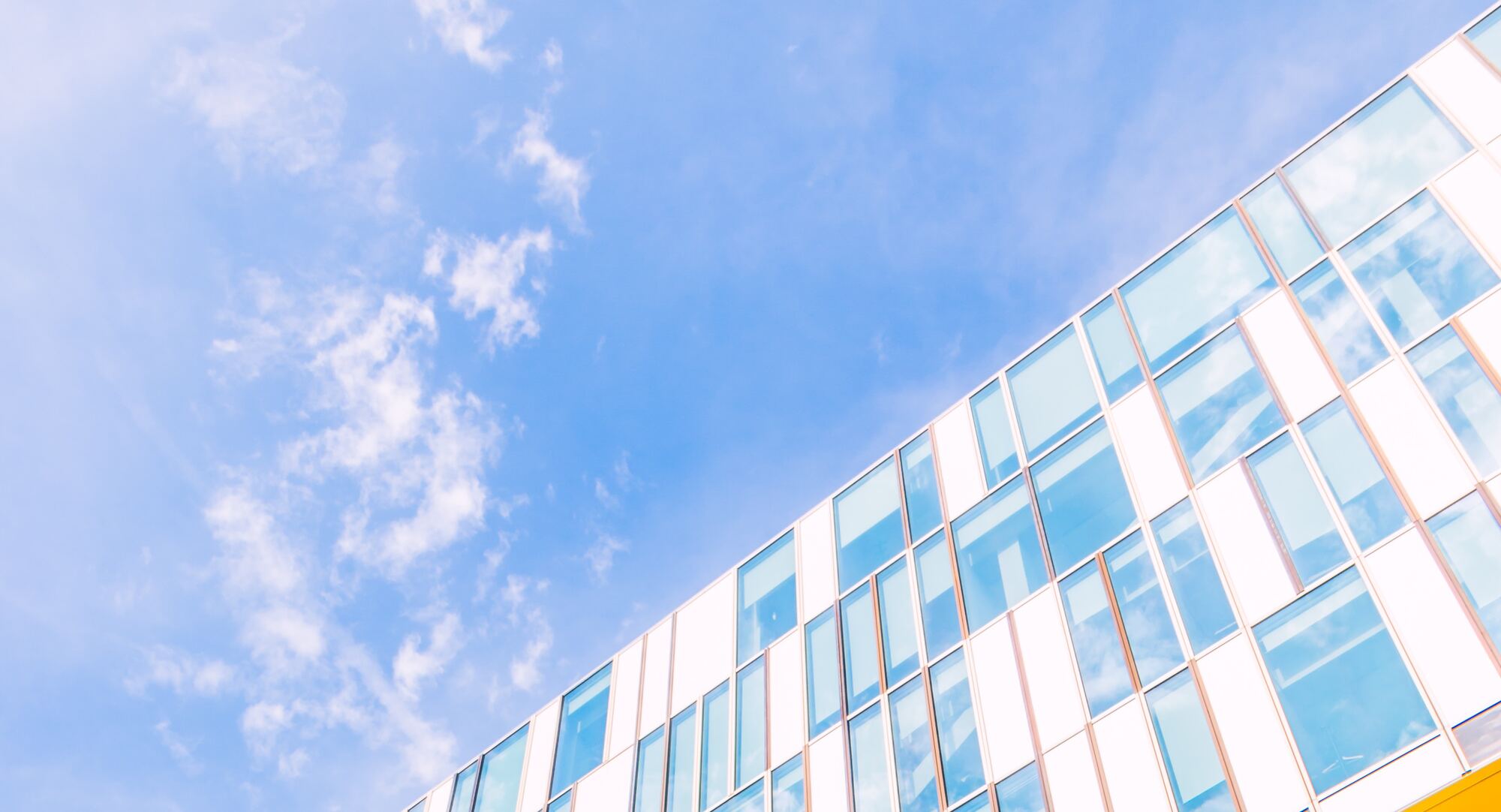 Façade vitrée de bureaux en diagonale, aux vitres reflétant un ciel bleu